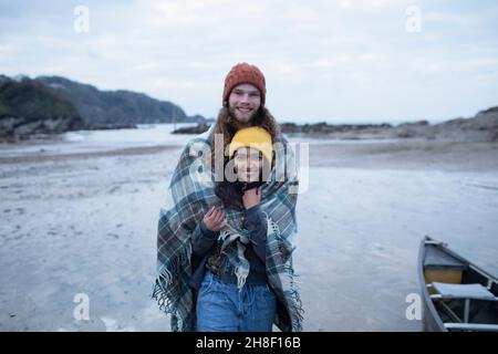 Portrait glückliches junges Paar in einer Decke am Strand gewickelt Stockfoto