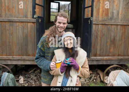 Portrait glückliches junges Paar, das vor der winzigen Hütte Kaffee trinkt Stockfoto