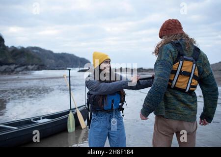 Junges Paar, das sich auf Kanufahrten am Strand vorbereitet Stockfoto