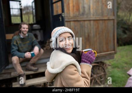 Glückliche junge Frau, die vor der winzigen Hütte Kaffee trinkt Stockfoto
