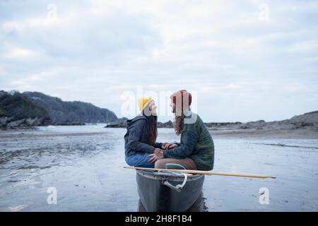 Glückliches junges Paar, das im Kanu am nassen Strand sitzt Stockfoto