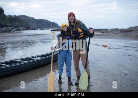 Portrait glückliches Paar mit Kanu und Rudern am Strand Stockfoto