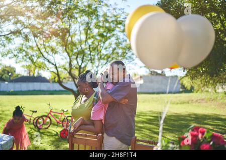 Großvater umarmt Enkelin im sonnigen Sommerhof Stockfoto