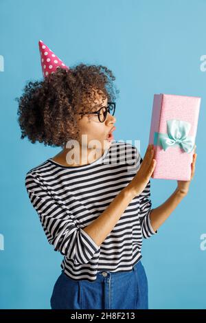 Staunende junge Frau im Geburtstagshut mit Geschenk Stockfoto