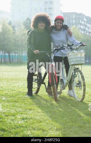 Portrait glückliches Teenager-Paar auf Fahrrädern im städtischen Parkgras Stockfoto