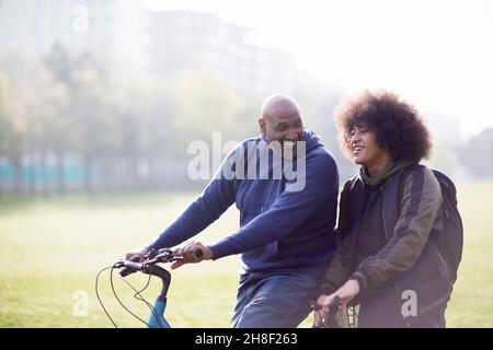 Glücklicher Vater und Sohn auf Fahrrädern im sonnigen Stadtpark Stockfoto