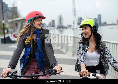 Glückliche junge Frauen Freunde in Helmen Fahrrad fahren in der Stadt Stockfoto