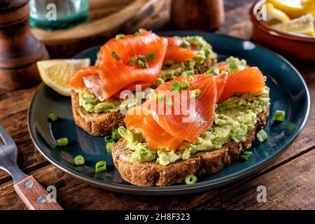 Köstliche Avocado- und Räucherlachs-Toasts auf einer rustikalen Holztischplatte. Stockfoto