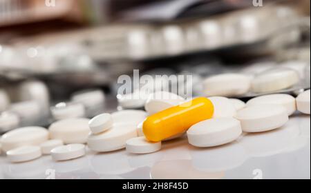 Gelbe Medikamentenkapsel zwischen weißen Tabletten Stockfoto