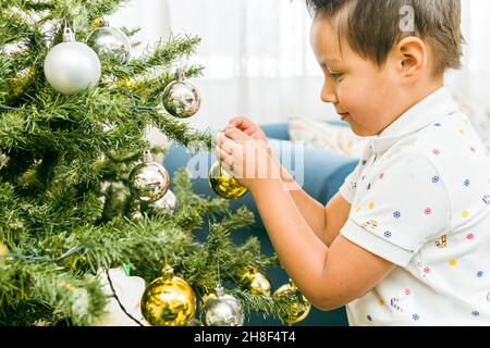 Hispanischer Junge, der zum Feiern einen Weihnachtsball auf einen Baum legt Stockfoto