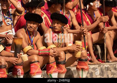 Naga-Stammesanwärter, die am 2. Dezember 2016 während des Hornbill-Festivals in Nagaland Indien in traditioneller Kriegerkleidung sitzen Stockfoto