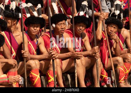 Naga-Stammesanwärter, die am 2. Dezember 2016 während des Hornbill-Festivals in Nagaland Indien in traditioneller Kriegerkleidung sitzen Stockfoto