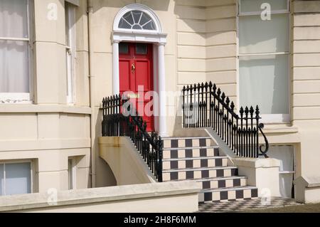 Außenansicht des Grundstücks mit einer roten Tür, schmiedeeisernen Geländern und schwarz-weißen Stufen, Brighton, East Sussex, England, Großbritannien Stockfoto