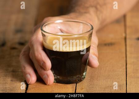 Mann griff mit der Hand ein kleines Glas Kaffee auf einem rustikalen Holztisch Stockfoto