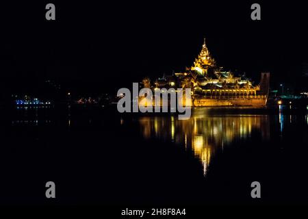 YANGON, MYANMAR (BURMA) - 19. Aug 2017: Karaweik Palace Hall Barge, beleuchtet golden hell in der Nacht reflektieren auf Kandawgyi See, Yangon, Myanmar, Burma Stockfoto