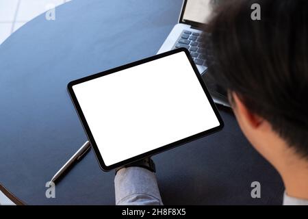 Nachbildung eines Geschäftsmannes, der in einem modernen Büro einen schwarzen Tablet-pc mit leerem weißen Bildschirm hält Stockfoto