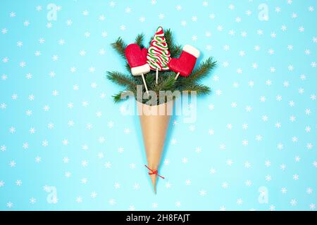 Geschenk grüne Tannenbaum in Handwerk Papiertüte mit Weihnachten Süßigkeiten und Schneeflocken auf blauem Hintergrund. Null-Abfall-Urlaubskonzept. Draufsicht. Flach liegend Stockfoto