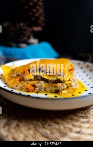 Scheibe gelbe Lasagne auf einem weißen Polka-Teller mit schwarzem Hintergrund Stockfoto