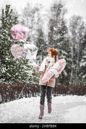 Junge happt hübsche Frau in stilvollen Pelzmantel und Fäustlinge zu Fuß mit Spielzeug Zauberstab und Glitzer Ballons in den Händen im Winter Park Stockfoto