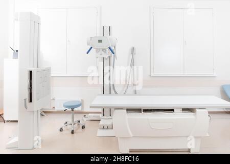 Röntgenabteilung im modernen Krankenhaus. Röntgenraum mit Scangerät und leerem Bett. Techniker, der ein Röntgengerät anpasst. Scannen von Brust, Herz Stockfoto