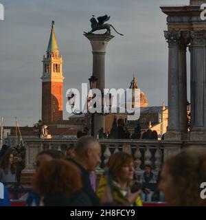 Blick auf die Bronzestatue auf dem markusplatz des geflügelten Löwen über einer Säule mit dem Glockenturm der St. Georges Kirche im Hintergrund Stockfoto