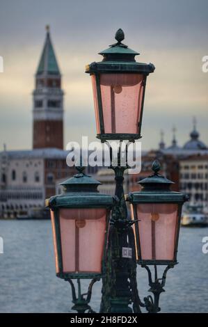 Nahaufnahme einer typischen venezianischen alten schmiedeeisernen Straßenlampe. San Marco Glockenturm im Hintergrund Stockfoto