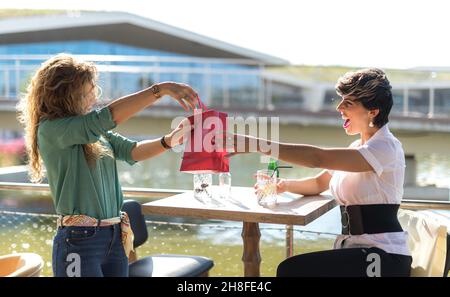 Zwei Freundinnen, die sich gegenseitig Geschenke geben und dabei glücklich überrascht werden Stockfoto