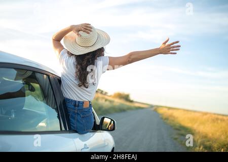 Mädchen mit einem Hut, der ihren Körper aus einem Autofenster ragt. Freiheit und Abenteuer Konzept. Stockfoto