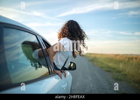 Mädchen, die ihren Körper aus einem Autofenster ragt. Freiheit und Abenteuer Konzept. Stockfoto