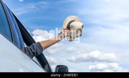 Die Hand einer Frau zieht einen Hut aus einem Autofenster. Freiheit, Reise- und Urlaubskonzept. Stockfoto