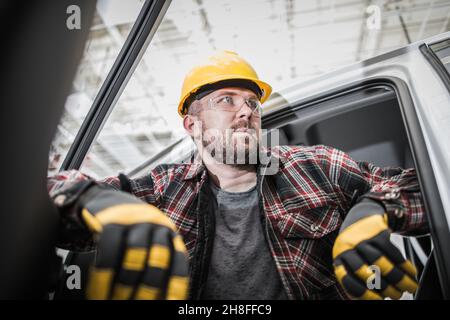 Kaukasischer Baustellenarbeiter in seinem 30s in seinem Pickup Truck. Männer tragen Schutzhelm, Brille und Arbeitshandschuhe. Stockfoto
