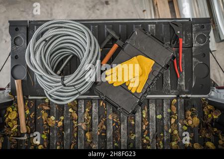 Elektriker Werkzeuge und Materialien auf einem Pickup Truck Bett Draufsicht. Metallgehäuse für elektrische Kabelschanentoduit und Werkzeuge. Herbstzeit Bauthema. Stockfoto