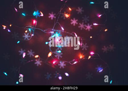 Schöne Glühende Weihnachten Hintergrund. Niedliche kleine Schneeflocken auf dunkler Kulisse mit bunten Festoon dekoriert. Frohes Neues Jahr Hintergrund. Stockfoto