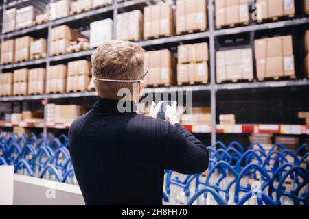 Junger Manager des Ladens, Arbeiter mit Schutzmaske, der Telefon benutzt, der in einer Industriefabrik oder einem Lager arbeitet. Stockfoto