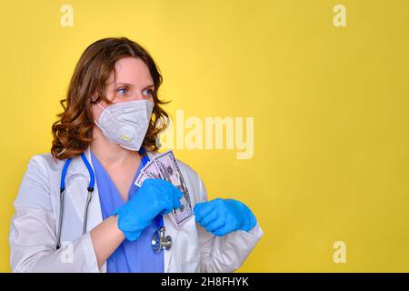 Ein Arzt behält ein Gehalt in US-Dollar, kopieren Sie Platz für Text. Eine Krankenschwester mit Geld für die Arbeit und einer Schutzmaske auf gelbem Hintergrund. Stockfoto