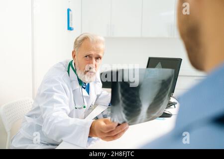 Nahaufnahme eines nicht erkennbaren männlichen Patienten, der einem erwachsenen Arzt zuhört, mit einer Röntgenaufnahme der Brust und einer ärztlichen Konsultation Stockfoto