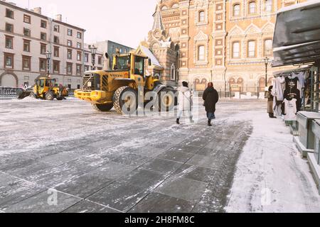 Sankt Petersburg, Russland - 16. Januar 2021: Gelber Traktor Volvo und Wille räumen den Schnee auf der Straße in der Nähe der Kirche des Erlösers auf Blut Stockfoto