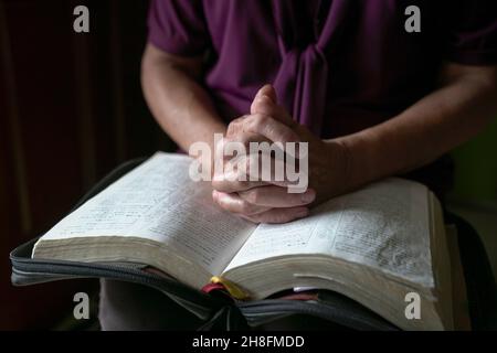 Nahaufnahme der älteren Frau Hände auf offene bibel, gefaltet im Gebet. Stockfoto