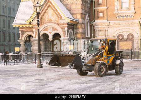 Sankt Petersburg, Russland - 16. Januar 2021: Gelber Traktor Wille nach Schneefall räumt die Straße und Straße in der Nähe der Kirche des Erlösers auf Blut Stockfoto