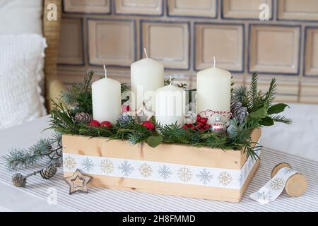 Adventsarrangement mit weißen Kerzen und grünen Zweigen in Holzkiste Stockfoto