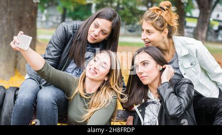 Glückliche Freundinnen sitzen auf der Parkbank und machen mit dem Handy Selbstgemachtes Stockfoto