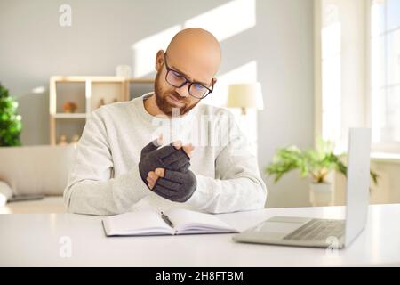 Mann, der an Arthritis leidet und an Schmerzen leidet und Kompressionshandschuhe trägt, während er am Computer arbeitet Stockfoto