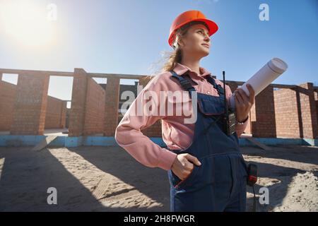 Triumnizende Baumeisterin mit vollem Gang, die in der Nähe von sonnenbeschienenen Gebäuden steht Stockfoto