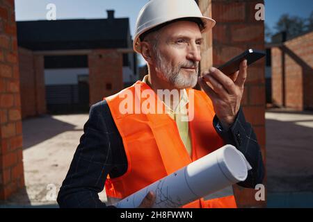 Serious Builder in Hardhat mit einem Gespräch am Telefon Stockfoto