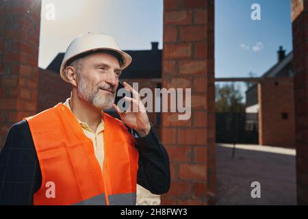 Fröhlicher Bauarbeiter, der ein Telefongespräch führt Stockfoto