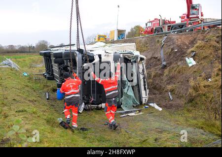 Padenstedt, Deutschland. 30th. November 2021. Mitarbeiter eines Bergungsunternehmens bereiten den abgestürzten Lkw mit einem schweren Kran zum Heben vor. Ein mit 22 Tonnen Schweinehälften beladener LKW durchbrach auf der Zufahrtsstraße von der B 205 zur B 7 bei Neumünster-Süd eine Leitplanke und ließ die Zufahrtsstraße stundenlang schließen. Quelle: Jonas Walzberg/dpa/Alamy Live News Stockfoto