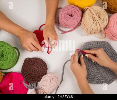 Draufsicht auf weibliche Hände mit Stricken auf einem weißen Tisch. Zwei Frauen stricken Körbe aus Baumwollgarn. Stockfoto