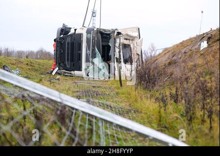 Padenstedt, Deutschland. 30th. November 2021. Der am Unfall beteiligte Lkw liegt im Graben neben der Zufahrtsstraße. Ein mit 22 Tonnen Schweinehälften beladener LKW hat auf der Zufahrtsstraße von der B 205 zur B 7 bei Neumünster-Süd eine Leitplanke durchbrochen, wodurch die Zufahrtsstraße stundenlang gesperrt wurde. Kredit: Jonas Walzberg/dpa - ACHTUNG: Nummernschild pixelated/dpa/Alamy Live Nachrichten Stockfoto