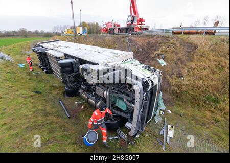 Padenstedt, Deutschland. 30th. November 2021. Mitarbeiter eines Bergungsunternehmens bereiten den abgestürzten Lkw mit einem schweren Kran zum Heben vor. Ein mit 22 Tonnen Schweinehälften beladener LKW durchbrach auf der Zufahrtsstraße von der B 205 zur B 7 bei Neumünster-Süd eine Leitplanke und ließ die Zufahrtsstraße stundenlang schließen. Kredit: Jonas Walzberg/dpa - ACHTUNG: Nummernschild pixelated/dpa/Alamy Live Nachrichten Stockfoto