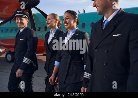 Lächelnde Flugzeugbesatzungsmitglieder, die auf der Landebahn zusammen laufen Stockfoto